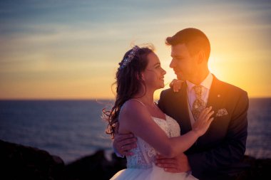 Düğünden sonra gün batımında okyanus kenarında damat ve gelin portresi.