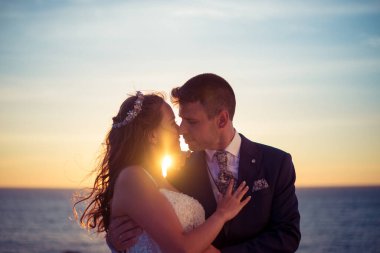 Düğünden sonra gün batımında okyanus kenarında damat ve gelin portresi.