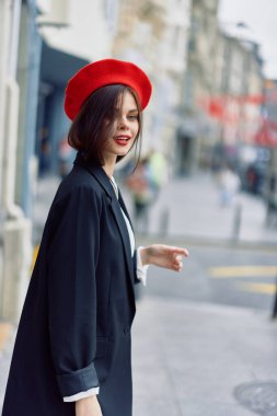 Moda kadını bahar aylarında şehirde kırmızı dudaklı, kırmızı bereli, gezgin, sinematik renk, eski moda tarzı, kentsel moda tarzıyla yürürken gülümser. Yüksek kalite fotoğraf