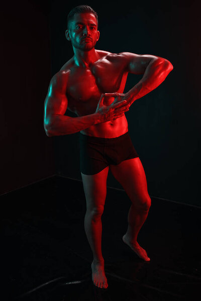Fashion portrait of an athletic trim attractive man. Manly naked torso in his underpants. Colored flash of studio neon light. High quality photo