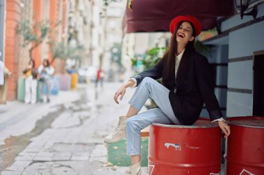 Dişleriyle gülümseyen güzel bir kadın, şehir caddesindeki bir kafenin önünde, şık bir moda elbisesi, tatili ve seyahati var. Yüksek kalite fotoğraf