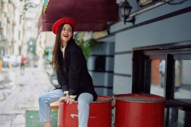 Güzel bir kadın, dişleriyle bir kafe ve barın önünde oturmuş gülümsüyor. Şık bir elbise, tatil ve seyahat. Yüksek kalite fotoğraf