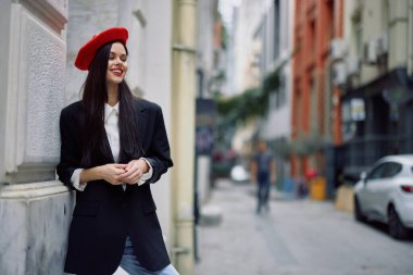 Şehirde bir duvarın yanında dikilen bir kadın şık bir ceket ve kırmızı dudaklı kırmızı bereli bir kadın seyahat ve boş zaman, Fransız tarzı elbise, bahar. Yüksek kalite fotoğraf