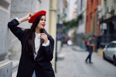 Şehirde bir duvarın yanında duran şık bir ceket ve kırmızı dudaklı kırmızı bereli bir kadın seyahat ediyor. Yüksek kalite fotoğraf