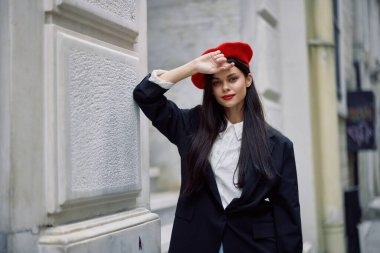 Şehirde bir duvarın yanında dikilen bir kadın şık bir ceket ve kırmızı dudaklı kırmızı bereli bir kadın seyahat ve boş zaman, Fransız tarzı elbise, bahar. Yüksek kalite fotoğraf