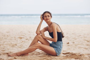 Sahil kenarında oturan bir kadın gülümseyerek sahil tatili ve Kafkas saç stili seksi özgürlük tasasız doğa seyahati uzun deniz tatili