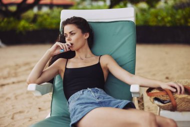 Bu kadın iskemle yaşam tarzı tatil beldesi yalancı esmer Kafkas güneş yatağı kumsalda gülümseyen okyanus gözlüklü su sandalyesi mavi kumlu mayo.