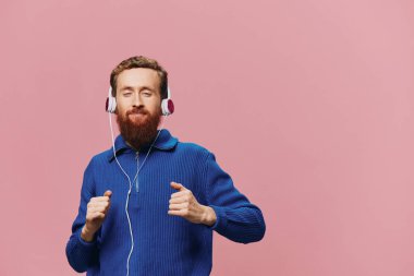 Kulaklık takan, gülümseyen ve dans eden, pembe arka planda müzik dinleyen kızıl saçlı bir adamın portresi. Sakallı bir hippi. Yüksek kalite fotoğraf