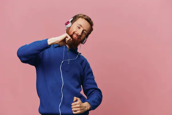 一个红头发男人的画像 戴着耳机 带着微笑和跳舞 听着粉色背景的音乐 一个留着胡子的嬉皮士高质量的照片 — 图库照片