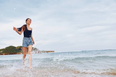 Günbatımında genç bir kadın, koşan bir kız, deniz suyu, seksi bir tatil, uzun bir yolculuk, yaz, mutluluk, sahil, tatil, özgürlük, uzay, yaşam tarzı gülümseme.