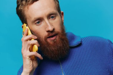 Elinde telefon olan bir adamın portresi mavi bir arka planda telefona bakıp konuşabiliyor. Çevrimiçi sosyal medya iletişimi, yaşam tarzı. Yüksek kalite fotoğraf