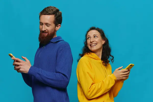 女人和男人快乐地结合在一起 手里拿着手机 弯下腰笑着 蓝蓝的背景 真正的家庭关系的概念 在电话里交谈 在网上工作 高质量的照片 — 图库照片