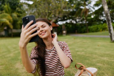 Kadın gülen palmiye ağacı cep telefonu güzel yetişkin parkı tişörtü yaşam tarzı telefon hücresi çizgili sağlıklı insan akıllı telefon doğa blogcusu kullanıyor.