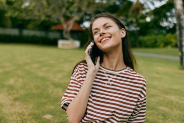Kadın mutlu bir konuşma Palm phone Spring doğa yaşam tarzı yaz parkı ağaç tişörtü blogcusu açık havada gülümseyen hücre mevsimsel kişi çim aramak