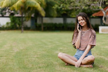 Kadın blogger Kafkas gömlek çalışan yetişkin ağaç mutlu telefon yaşam tarzı Palmiye yeşili çimen park genç çanta sağlıklı ağ gülümseyen mobil