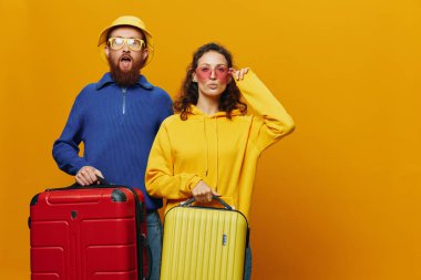 Kadın ve erkek gülümsüyor, ellerinde sarı ve kırmızı bavullar neşeyle ve çarpık bir şekilde gülümsüyor, sarı arka plan, seyahate çıkıyor, aile tatili, yeni evliler. Yüksek kalite fotoğraf
