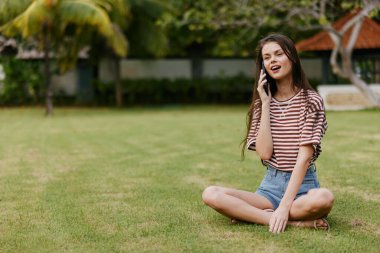 Dışarıdaki kadın palmiye kızı yaşam tarzı yeşil çanta kadın çim konuşuyor blogcu telefon oturuyor gülümseyen bahar parkı sağlıklı yürüyüş mutlu tarama