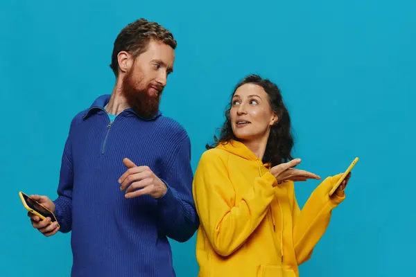 女性と男性は 彼らの手で携帯電話を持つ陽気なカップルは 青い背景に笑顔を浮かべました 実際の家族関係の概念 電話で話す オンラインで動作する 高品質の写真 — ストック写真