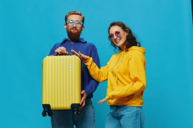 Kadın ve erkek, çantanın üzerinde oturmuş gülümsüyor. Sarı bavul gülüşü, mavi arka plan, yolculuk için toplanma, aile tatili. Yüksek kalite fotoğraf