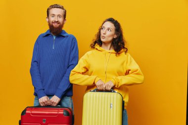 Kadın ve erkek gülümsüyor, ellerinde sarı ve kırmızı bavullar neşeyle ve çarpık bir şekilde gülümsüyor, sarı arka plan, seyahate çıkıyor, aile tatili, yeni evliler. Yüksek kalite fotoğraf