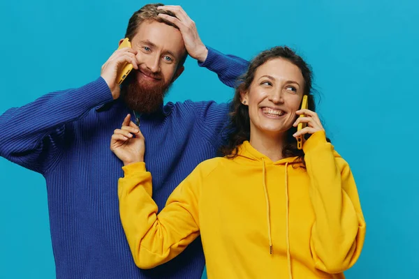 Kadın ve erkek, ellerinde telefon olan neşeli bir çift. Mavi arka planda, çarpık bir gülümseme. Gerçek aile ilişkileri kavramı, telefonda konuşmak, internette çalışmak. Yüksek kalite fotoğraf