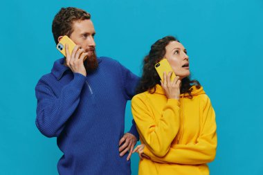 Kadın ve erkek, ellerinde telefon olan neşeli bir çift. Mavi arka planda, çarpık bir gülümseme. Gerçek aile ilişkileri kavramı, telefonda konuşmak, internette çalışmak. Yüksek kalite fotoğraf