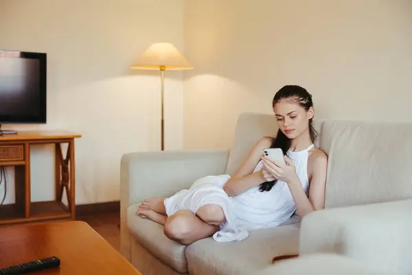 一位年轻女性坐在客厅的沙发上 手里拿着手机 轻松地在线工作和社交媒体自由撰稿人 高质量的照片 — 图库照片