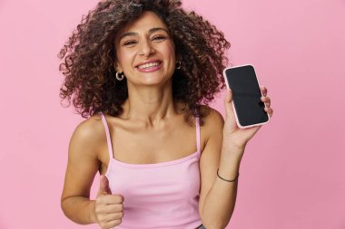 Telefon görüşmesi yapan kadın blogcu, pembe tişörtlü kıvırcık saçlı ve kot pantolonlu selfie çekiyor. Pembe arka planda, fotokopi alanında, teknolojide ve sosyal medyada poz veriyor. Yüksek kalite fotoğraf