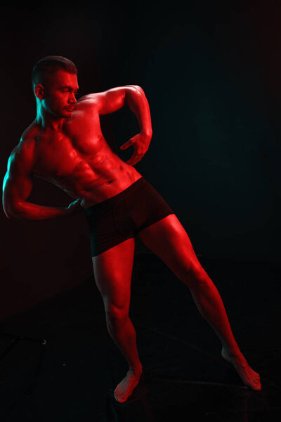 Man bodybuilder athlete with bare torso fashion pose on black isolated background with colored light neon red and green. The concept of a healthy male body sport. High quality photo