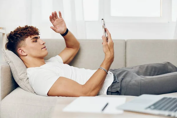 男人坐在室内用笔记本电脑生活方式电话沙发人十几岁的时候在家模仿互联网男人在线发短信技术 — 图库照片
