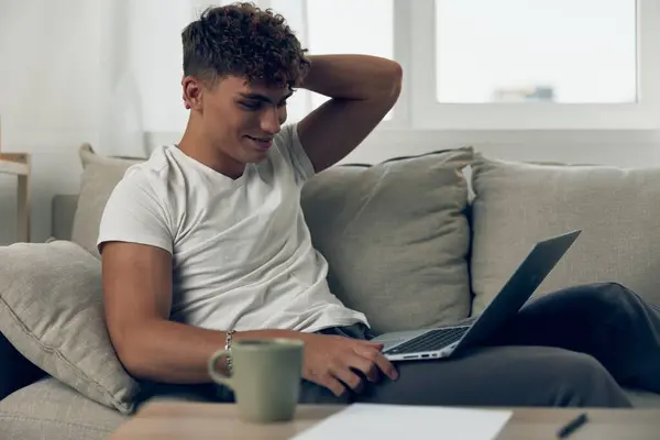 男人电脑无线使用电话T恤坐在网上聊天教育快乐的工作笔记本电脑网络空间技术看起来像笔记本电脑的学生 — 图库照片