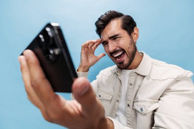Sinirli ve sinirli sakallı telefon blogcusuna bakan şık esmer bir adamın portresi. Oyunu beyaz tişört ve kot pantolon içinde mavi bir arka planda kaybediyor. Kopya alanı. Yüksek kalite fotoğraf