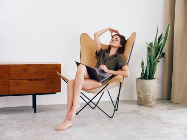 Kız öğrenci eğitimi, evinde dizüstü bilgisayarı olan bir sandalyede oturuyor gülümse ve rahatla, modern İskandinav tarzı iç mimari yaşam tarzı, kopyalama alanı. Yüksek kalite fotoğraf