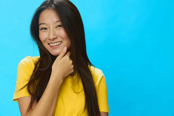 青い背景に黄色いTシャツと青いジーンズの緩い背景で指を指して歯で微笑むアジアの女性 コピースペース 高品質の写真 — ストック写真