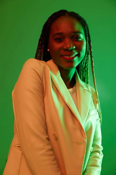 African american woman portrait business smile on green background in neon light, color mixed light, bright colors. Beauty African American woman with pigtails emotions. High quality photo