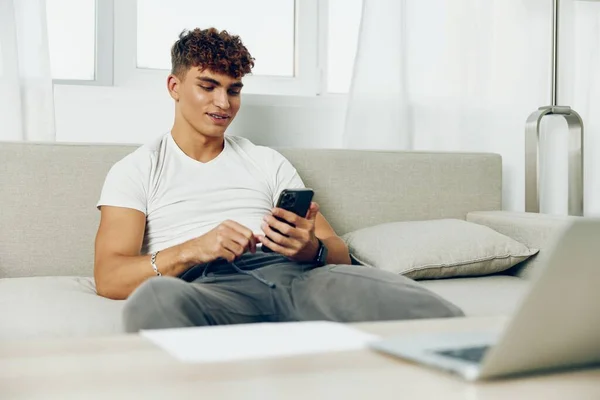 男人在室内卷曲使用手机在线生活年轻的电话回家自己的文字业务模仿技术沙发信息自由职业者 — 图库照片