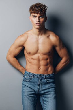 Genç kaslı, kaslı, gri arka plan seksi, ayakta duran kot pantolonlar sağlıklı, sporcu, erkek bakımı
