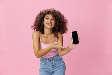 Telefon görüşmesi yapan kadın blogcu, pembe tişörtlü kıvırcık saçlı ve kot pantolonlu selfie çekiyor. Pembe arka planda, fotokopi alanında, teknolojide ve sosyal medyada poz veriyor. Yüksek kalite fotoğraf