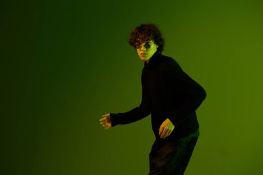 Gözlüklü erkek dansçı moda ve tarz duygu modeli dans, hipster gençlik yaşam tarzı, portre yeşil arka plan karışık neon ışığı, fotokopi alanı. Yüksek kalite fotoğraf