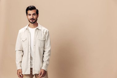 Beyaz tişört ve iş ceketiyle bej bir arka planda şık bir adam gülümsüyor, uçan kıyafet kahramanı, modaya uygun giyim tarzı, kopyalama alanı, mesaj için yer. Yüksek kalite fotoğraf