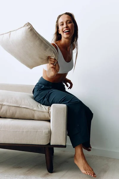 A woman with long hair plays with a pillow sitting on the couch at home and smiles. High quality photo
