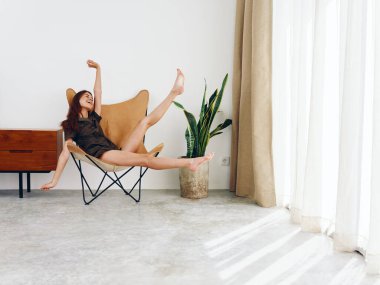 Pencere kenarında oturan bir kadın neşeli ayaklar ve eller yukarı, modern İskandinav tarzı iç mekan, kopyalama alanı. Yüksek kalite fotoğraf