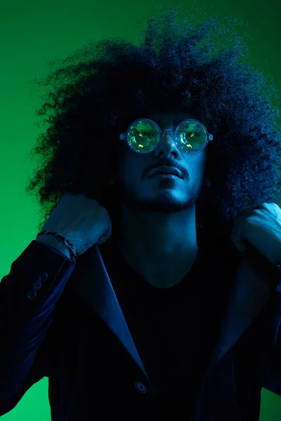 stock image Fashion portrait of a man with curly hair on a green background with sunglasses, multinational, colored pink light, trendy, modern concept. High quality photo