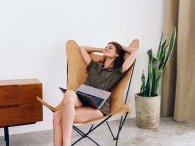 Sandalyesinde oturan serbest çalışan bir kadın öğrenci evinde dizüstü bilgisayarla çalışıyor gülümse ve rahatla, modern stil İskandinav yaşam tarzı, kopyalama alanı. Yüksek kalite fotoğraf