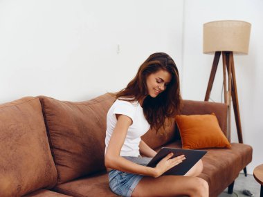 Kanepede oturan serbest çalışan bir kadın güzel bir dizüstü bilgisayarla gülümsüyor, modern stil bir İskandinav yaşam tarzı, kopyalama alanı. Yüksek kalite fotoğraf