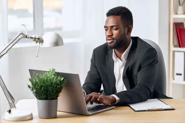 男の従業員のオフィスインターネット笑顔コンピュータオンラインアフリカのノートパソコンのテーブルのフリーランサーの学生の仕事アメリカの仕事黒い屋内ビジネスサイバースペース教育 — ストック写真