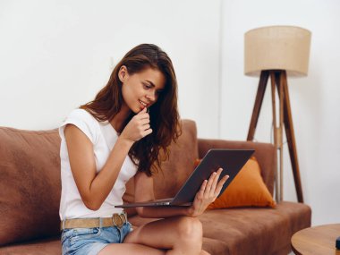 Kanepede oturan serbest çalışan bir kadın güzel bir dizüstü bilgisayarla gülümsüyor, modern stil bir İskandinav yaşam tarzı, kopyalama alanı. Yüksek kalite fotoğraf