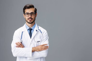 Beyaz önlüklü, görüş için gözlüklü ve steteskop takmış bir erkek doktor kameraya bakar. Gri izole arka planda diş hekimi ile gülümser. Kopya alanı, mesaj için yer, sağlık. Yüksek kalite fotoğraf