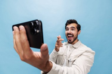 Şık, esmer bir adamın portresi sürpriz ve ağzı açık beyaz tişört ve kot pantolon içinde mavi arka planda sakallı telefon blogcusuna bakıyor. Yüksek kalite fotoğraf