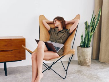 Sandalyesinde oturan serbest çalışan bir kadın öğrenci evinde dizüstü bilgisayarla çalışıyor gülümse ve rahatla, modern stil İskandinav yaşam tarzı, kopyalama alanı. Yüksek kalite fotoğraf